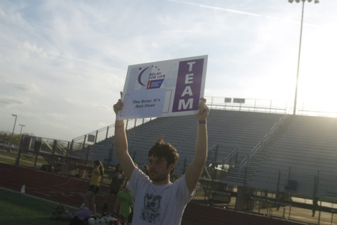 Senior Carter Benno proudly holds up his teams sign at dusk during Relay for Life on Friday, April 11, 2014.